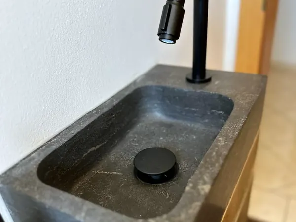 Kleines Handwaschbecken aus dunklem Stein mit schwarzer Armatur – Badsanierung, Kärnten
