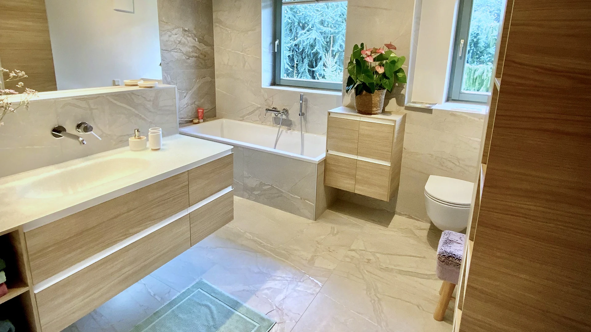 Modernes helles Badezimmer mit schwebendem Holz-Waschtisch, Badewanne und großformatigen Fliesen – Badsanierung, Kärnten