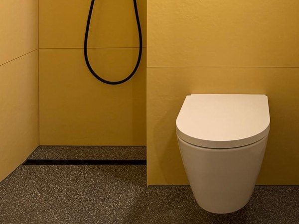 Bodengleiche Dusche mit Duschrinne und Wand-WC vor gelben Großformatfliesen